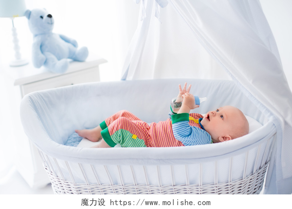 婴儿在婴儿床与冠层中用瓶子喝水Little baby with bottle in white bed